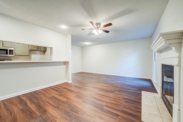 unfurnished living room featuring a textured ceiling, dark hardwood / wood-style floors, and ceiling fan