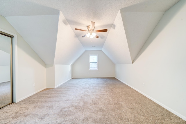 additional living space with light carpet, a textured ceiling, vaulted ceiling, and ceiling fan