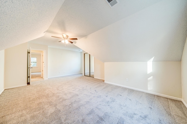 additional living space featuring light carpet, a textured ceiling, lofted ceiling, and ceiling fan