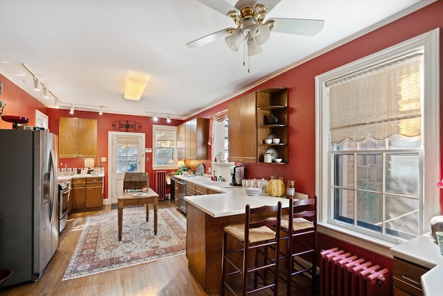 kitchen with wood-type flooring, kitchen peninsula, appliances with stainless steel finishes, radiator, and a kitchen breakfast bar