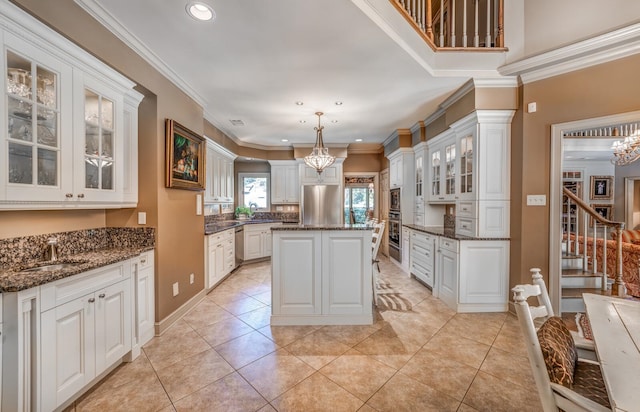 kitchen with hanging light fixtures, white cabinets, a kitchen island, crown molding, and sink