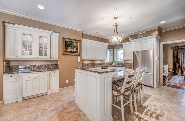 kitchen featuring pendant lighting, white cabinets, a kitchen island, stainless steel refrigerator, and crown molding