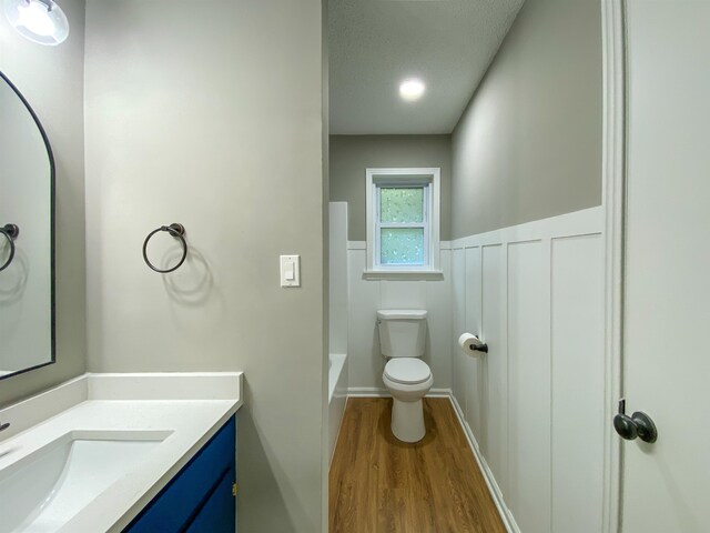 full bathroom with toilet, plus walk in shower, hardwood / wood-style flooring, vanity, and a textured ceiling