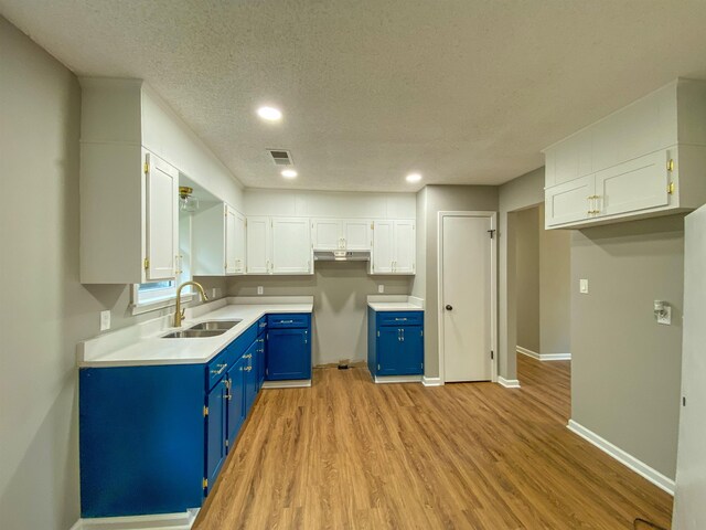 kitchen featuring blue cabinets, white cabinets, sink, a textured ceiling, and light wood-type flooring