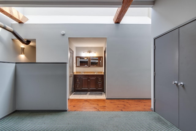 unfurnished bedroom with ensuite bathroom, beamed ceiling, and light colored carpet