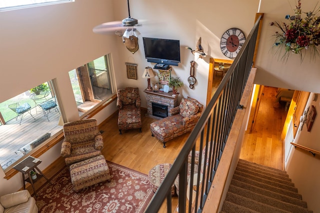 living room featuring wood-type flooring, a fireplace, a towering ceiling, and ceiling fan