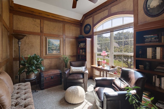 sitting room featuring carpet floors, wood walls, and ceiling fan