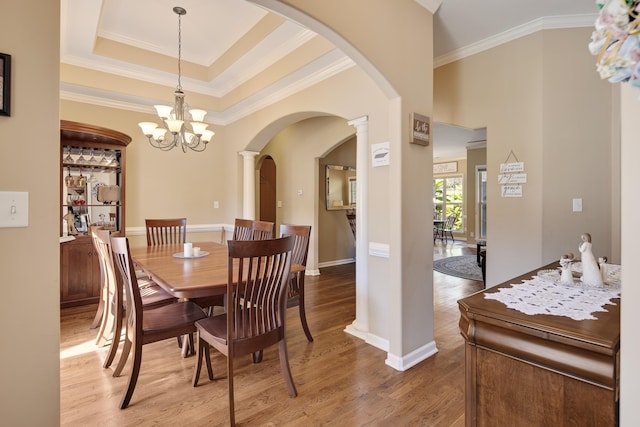 dining space featuring a raised ceiling, ornamental molding, wood-type flooring, a chandelier, and decorative columns