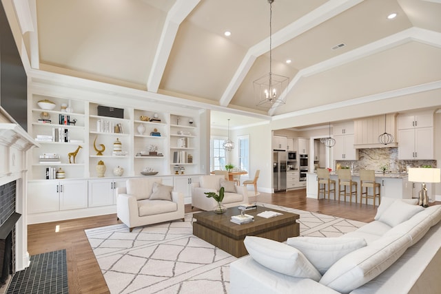 living room featuring light hardwood / wood-style flooring, a chandelier, vaulted ceiling with beams, and a brick fireplace