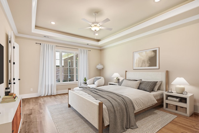 bedroom with ceiling fan, light hardwood / wood-style floors, and a raised ceiling