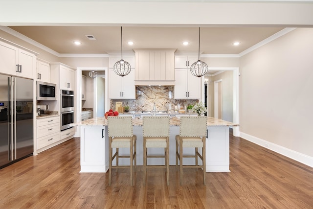 kitchen featuring decorative light fixtures, light stone countertops, white cabinets, appliances with stainless steel finishes, and a center island