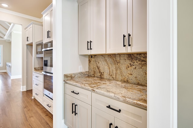 kitchen featuring light stone counters, tasteful backsplash, light hardwood / wood-style flooring, white cabinetry, and crown molding