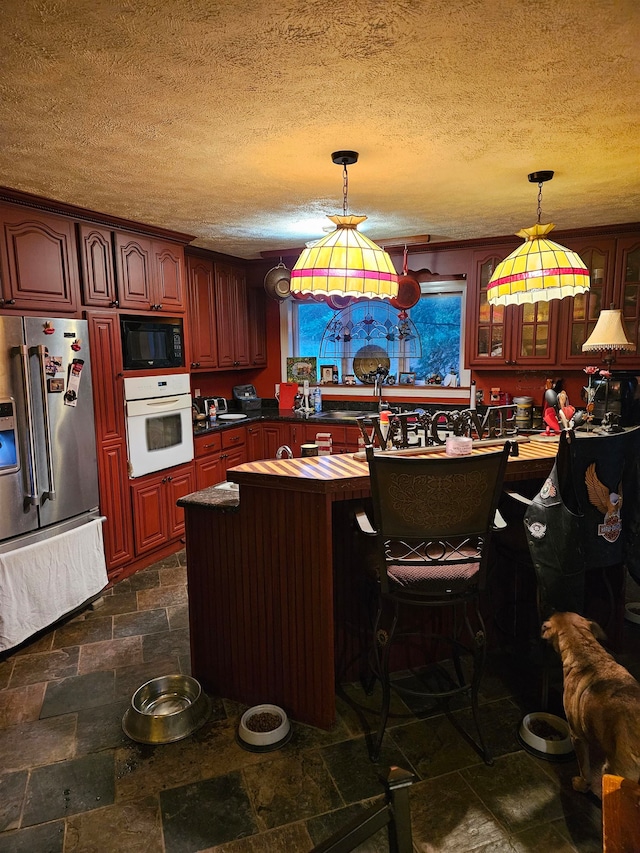 kitchen with decorative light fixtures, stainless steel fridge, oven, and black microwave