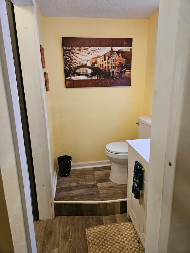 bathroom with a textured ceiling, wood-type flooring, vanity, and toilet