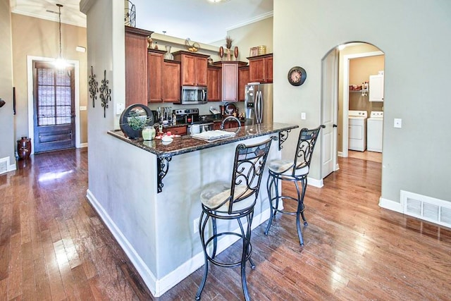 kitchen with a kitchen breakfast bar, appliances with stainless steel finishes, dark wood-type flooring, and decorative light fixtures