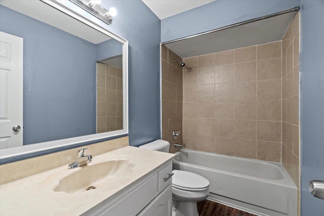 full bathroom with tiled shower / bath, vanity, toilet, a textured ceiling, and hardwood / wood-style floors