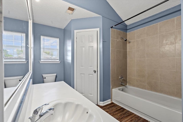 full bathroom featuring tiled shower / bath, hardwood / wood-style flooring, toilet, and a textured ceiling