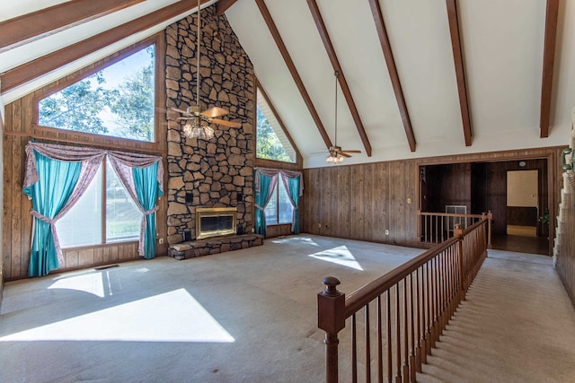 carpeted living room with ceiling fan, beam ceiling, a stone fireplace, wooden walls, and high vaulted ceiling