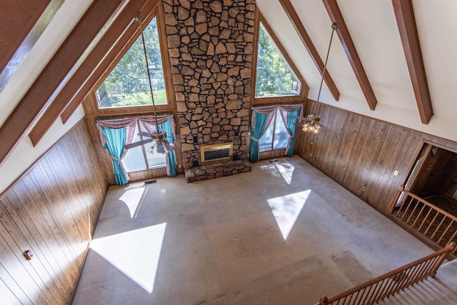 unfurnished living room with beam ceiling, high vaulted ceiling, wooden walls, and a healthy amount of sunlight