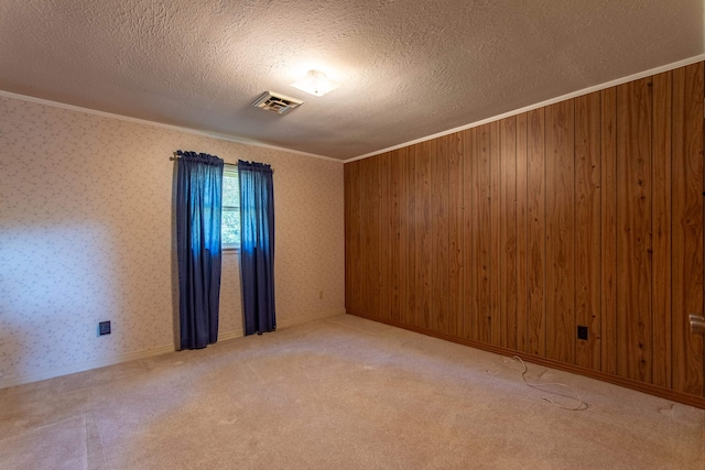 carpeted spare room with a textured ceiling, wood walls, and ornamental molding