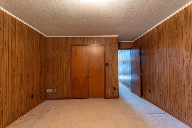 unfurnished bedroom with wood walls, a closet, ornamental molding, and light carpet