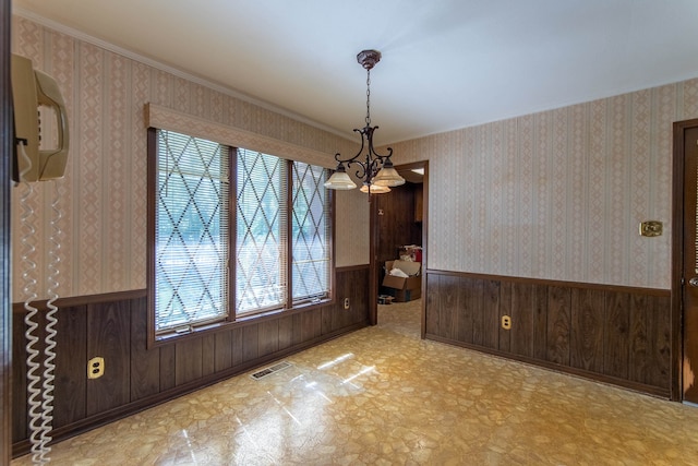 unfurnished dining area featuring ornamental molding, wooden walls, and a chandelier