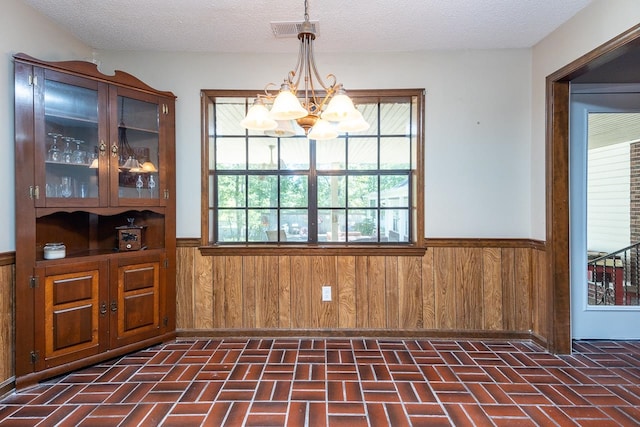 unfurnished dining area with a textured ceiling, wood walls, a chandelier, and plenty of natural light