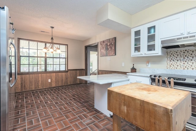 kitchen with wood walls, hanging light fixtures, white cabinets, and stove