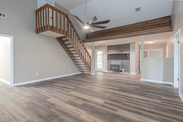 unfurnished living room featuring wood-type flooring, ceiling fan, a wood stove, and high vaulted ceiling