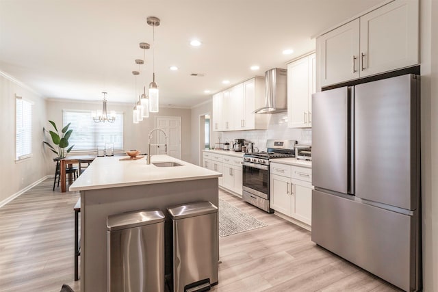 kitchen featuring wall chimney range hood, pendant lighting, sink, stainless steel appliances, and white cabinetry