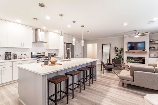 kitchen with appliances with stainless steel finishes, pendant lighting, wall chimney range hood, and white cabinetry