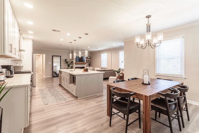 dining space featuring sink, light hardwood / wood-style flooring, ornamental molding, and a healthy amount of sunlight