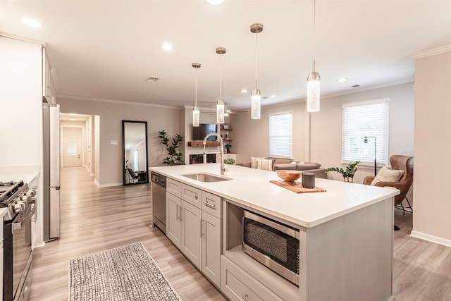 kitchen featuring light hardwood / wood-style floors, a center island with sink, sink, stainless steel appliances, and hanging light fixtures