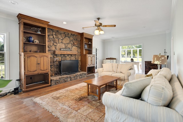 living room featuring a stone fireplace, light hardwood / wood-style flooring, ornamental molding, and ceiling fan