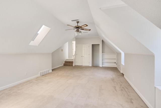 bonus room with lofted ceiling with skylight, light carpet, ceiling fan, and built in shelves