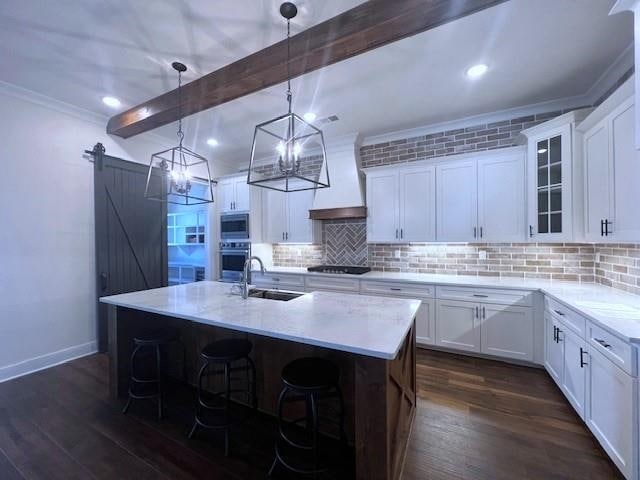 kitchen featuring a kitchen island with sink, white cabinets, dark hardwood / wood-style floors, a barn door, and beam ceiling