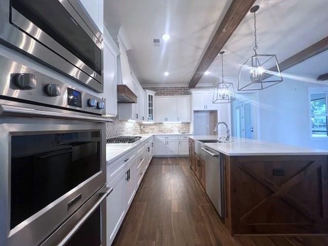 kitchen with stainless steel appliances, sink, beam ceiling, an inviting chandelier, and white cabinetry