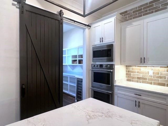 kitchen featuring white cabinetry, tasteful backsplash, a barn door, light stone counters, and appliances with stainless steel finishes