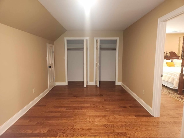 unfurnished bedroom featuring vaulted ceiling, two closets, and hardwood / wood-style floors