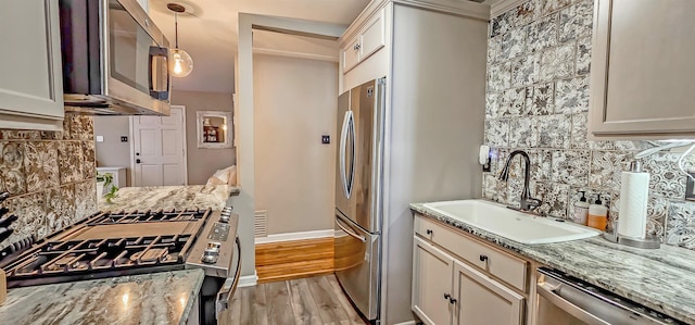 kitchen with pendant lighting, sink, light stone countertops, light hardwood / wood-style floors, and stainless steel appliances