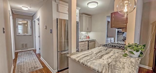 kitchen with pendant lighting, washer and clothes dryer, light stone counters, and appliances with stainless steel finishes