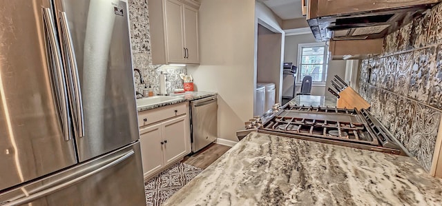 kitchen with sink, stainless steel appliances, washing machine and dryer, light stone counters, and light wood-type flooring