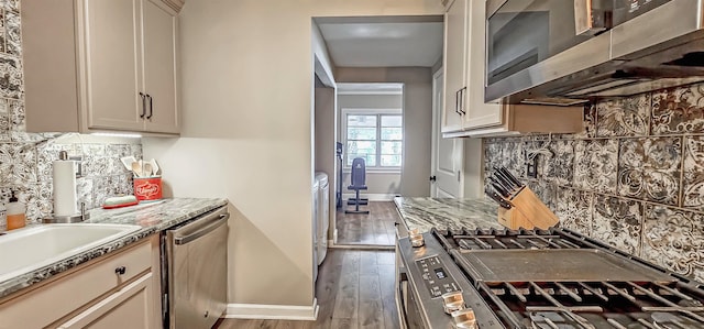 kitchen with tasteful backsplash, light stone counters, dark hardwood / wood-style floors, cream cabinetry, and appliances with stainless steel finishes