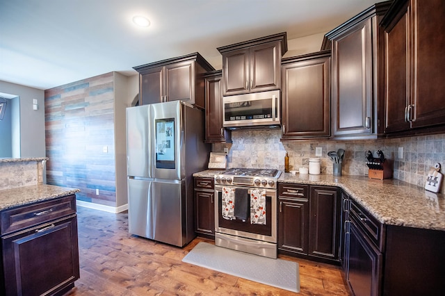 kitchen featuring light wood-type flooring, tasteful backsplash, dark brown cabinets, light stone countertops, and appliances with stainless steel finishes