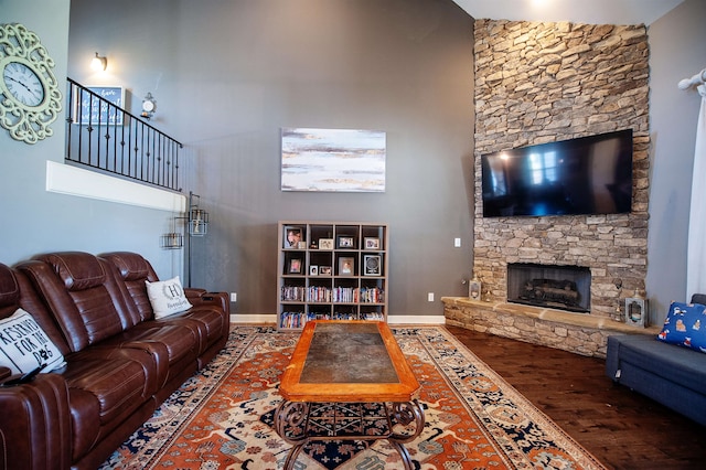 living room with wood-type flooring, a stone fireplace, and a high ceiling