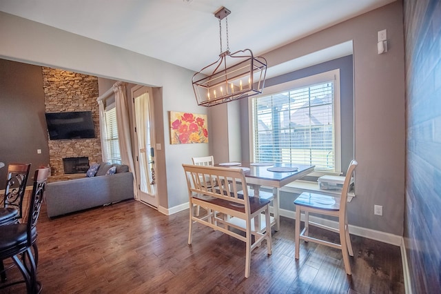 dining area featuring dark wood-type flooring, a notable chandelier, and a stone fireplace