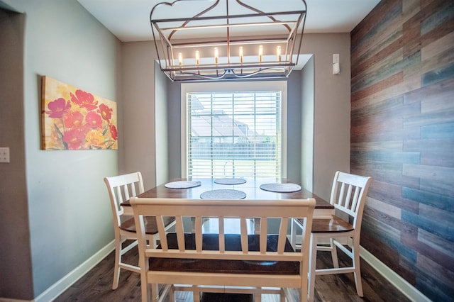 dining space with a notable chandelier, wooden walls, and dark wood-type flooring