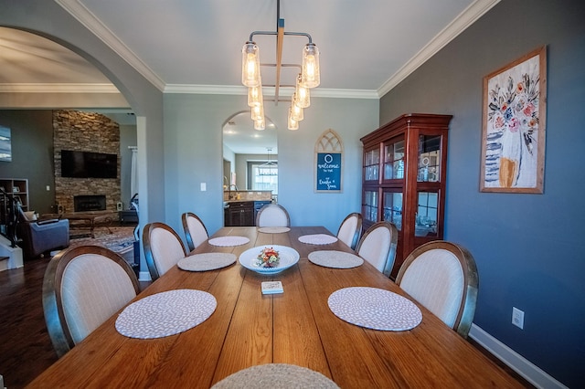 dining area with ornamental molding, sink, a stone fireplace, and ceiling fan with notable chandelier