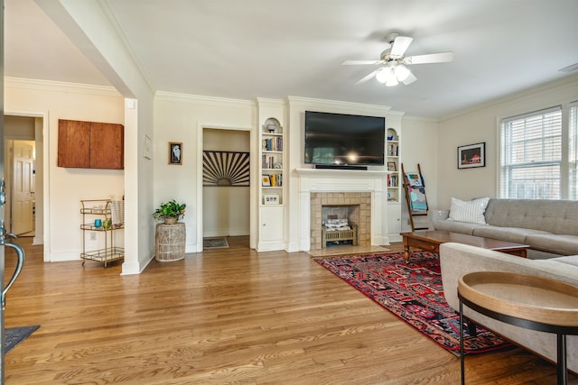 living room with a tiled fireplace, crown molding, hardwood / wood-style floors, and ceiling fan