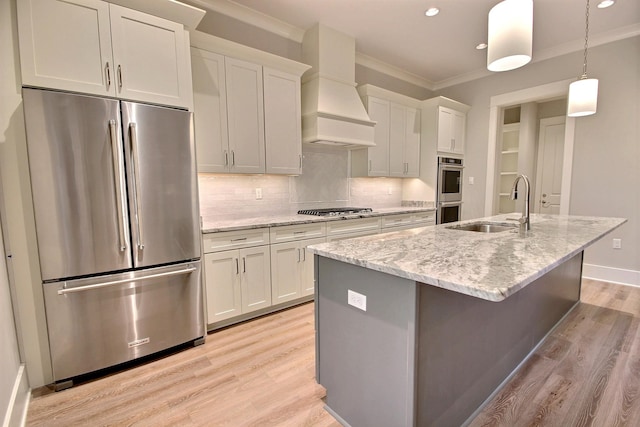 kitchen with light stone countertops, a kitchen island with sink, stainless steel appliances, custom range hood, and white cabinetry